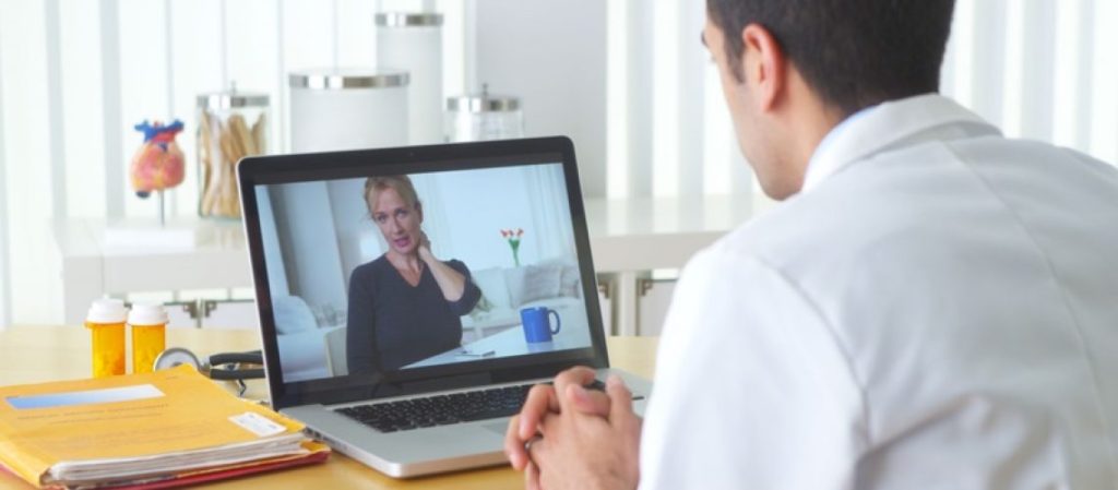 Homem de frente ao computador em uma sala tendo atendido atendimento médico online através de videochamada