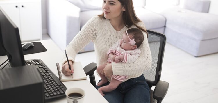 Mãe com bebê no colo e trabalhando