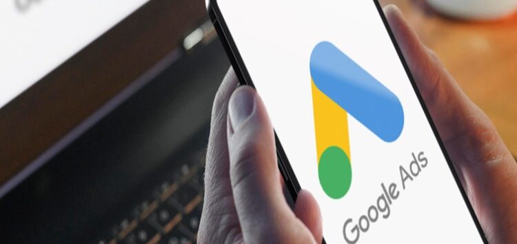 Imagem de uma pessoa em frente ao notebook e com um celular na mão e na tela do celular a logomarca do google adwords